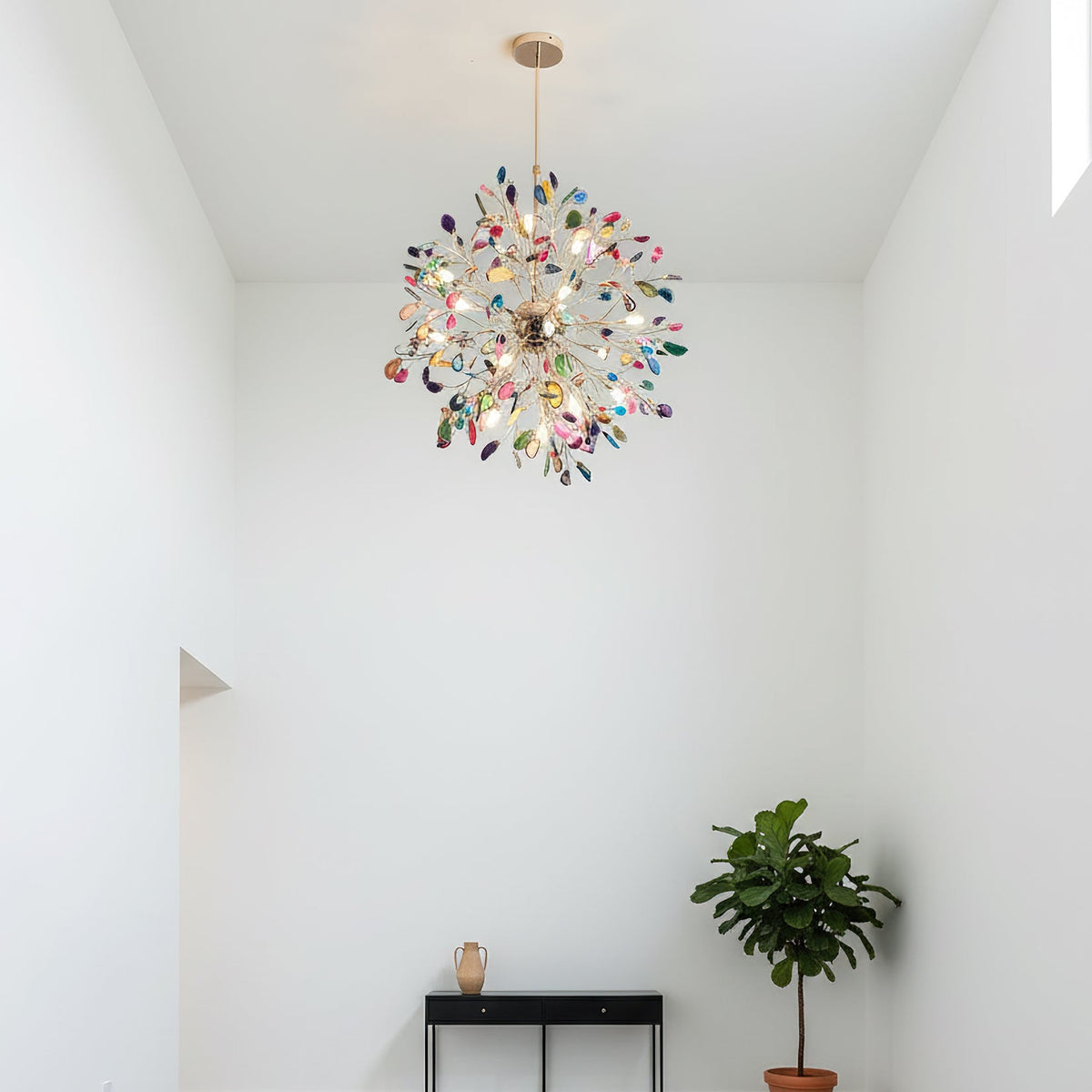 Lit Clérachic agate chandelier in a white room with a high ceiling, above a black console, a fig tree and a small vase.