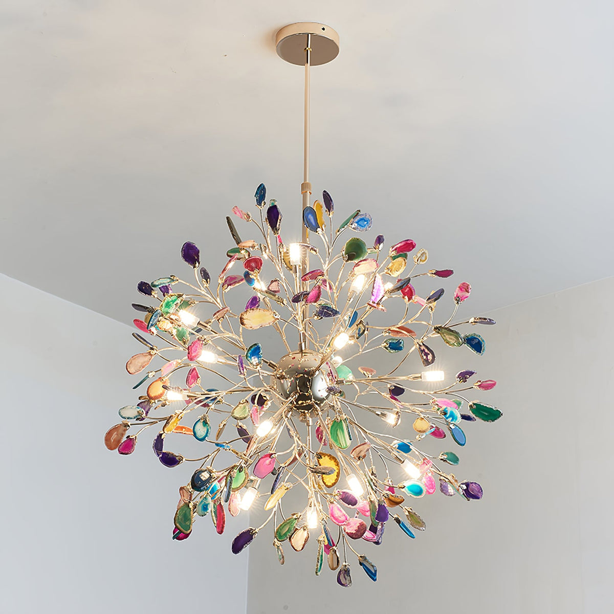 Close view from below of a lit Clérachic agate chandelier, its bulbs shining through slices in pink, green, blue and amber.