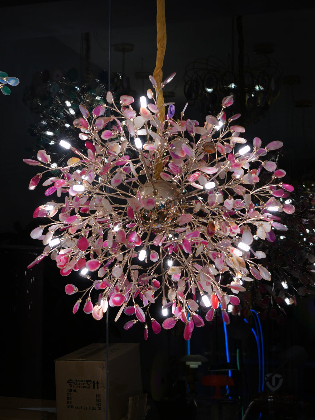 Lit Clérachic chandelier with pink agate slices on gold branches, photographed in a dark room.