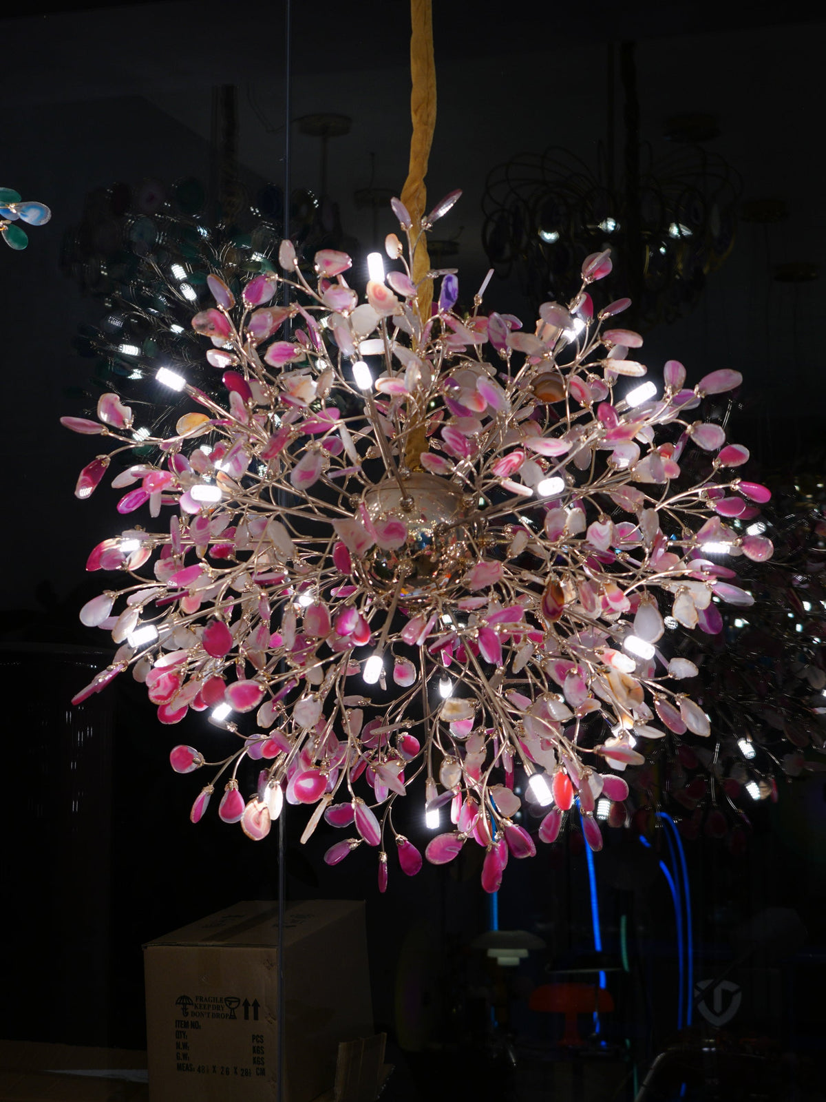 Lit Clérachic chandelier with pink agate slices on gold branches, photographed in a dark room.