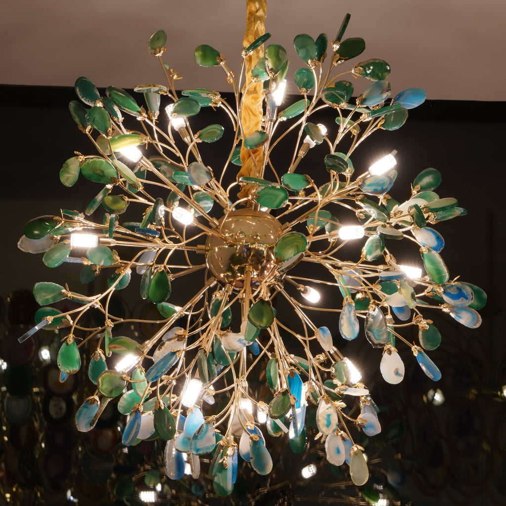Lit Clérachic chandelier with green and blue agate slices, seen from below in a dim room with bulbs shining between the leaves.