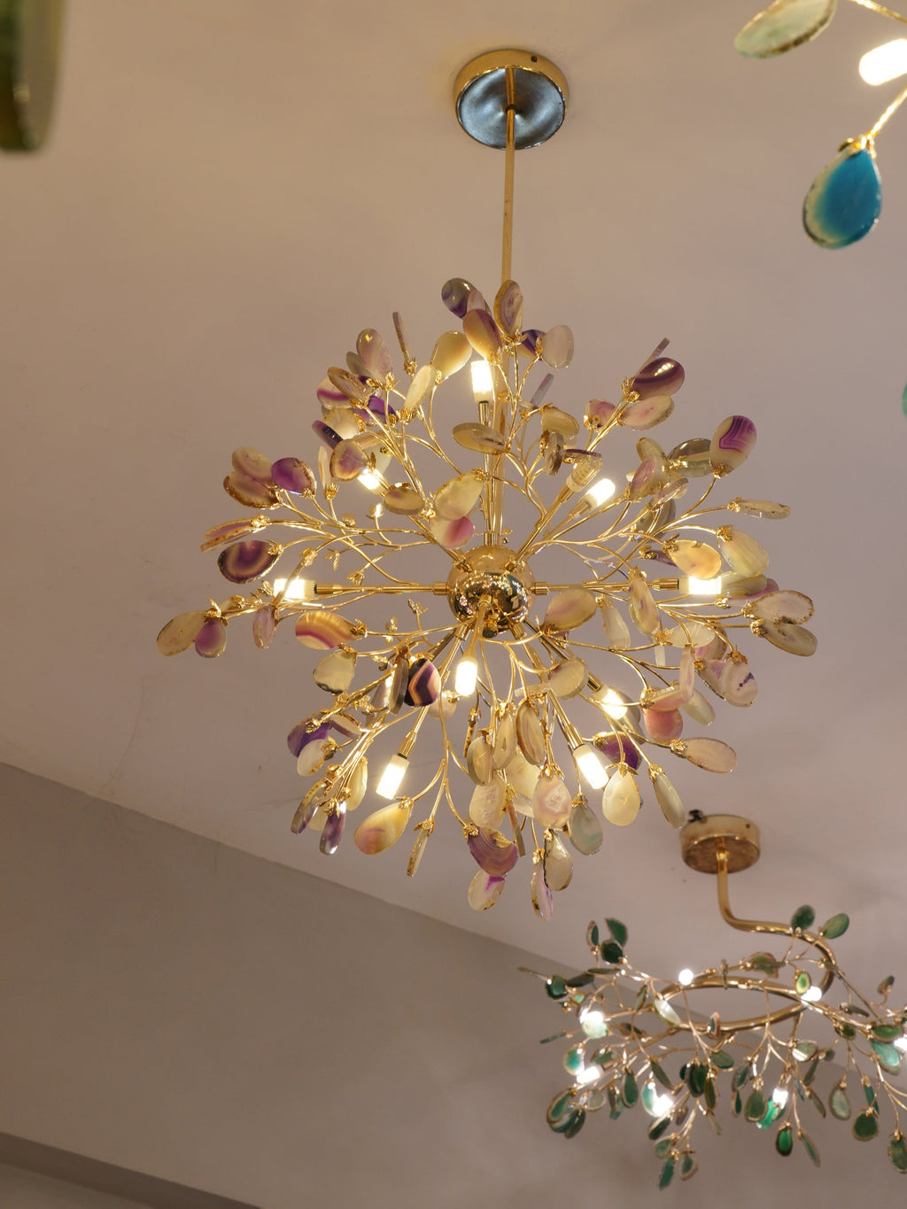 A Clérachic agate chandelier lit on a plaster ceiling, with a second chandelier of glass-like slices in the corner of the frame.