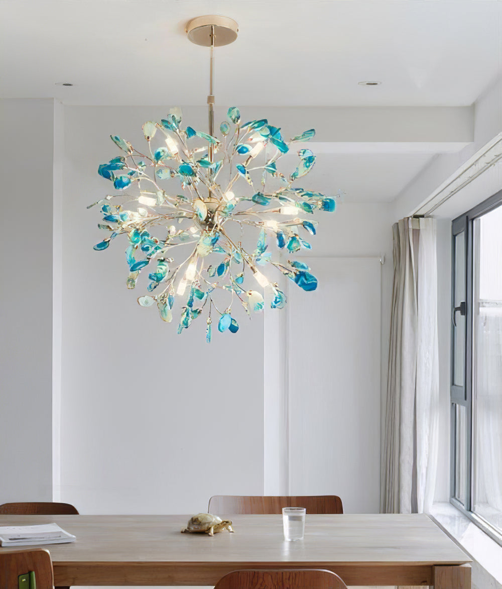 Blue-green agate Clérachic chandelier above a wooden dining table by a window with a sheer curtain.