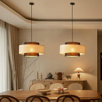 A pair of Clérachic rattan pendants glows above a wooden dining table, with a sideboard and a pleated table lamp behind.