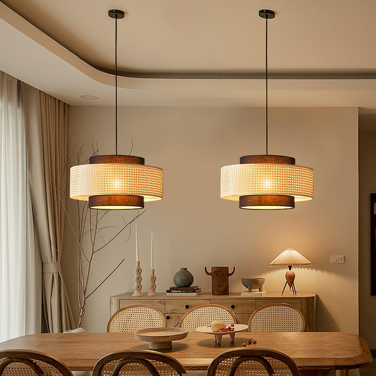 A pair of Clérachic rattan pendants glows above a wooden dining table, with a sideboard and a pleated table lamp behind.
