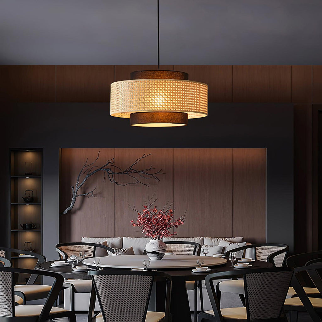 A rattan-banded Clérachic pendant hangs over a round dark table in a moody dining room with a dark wood wall.