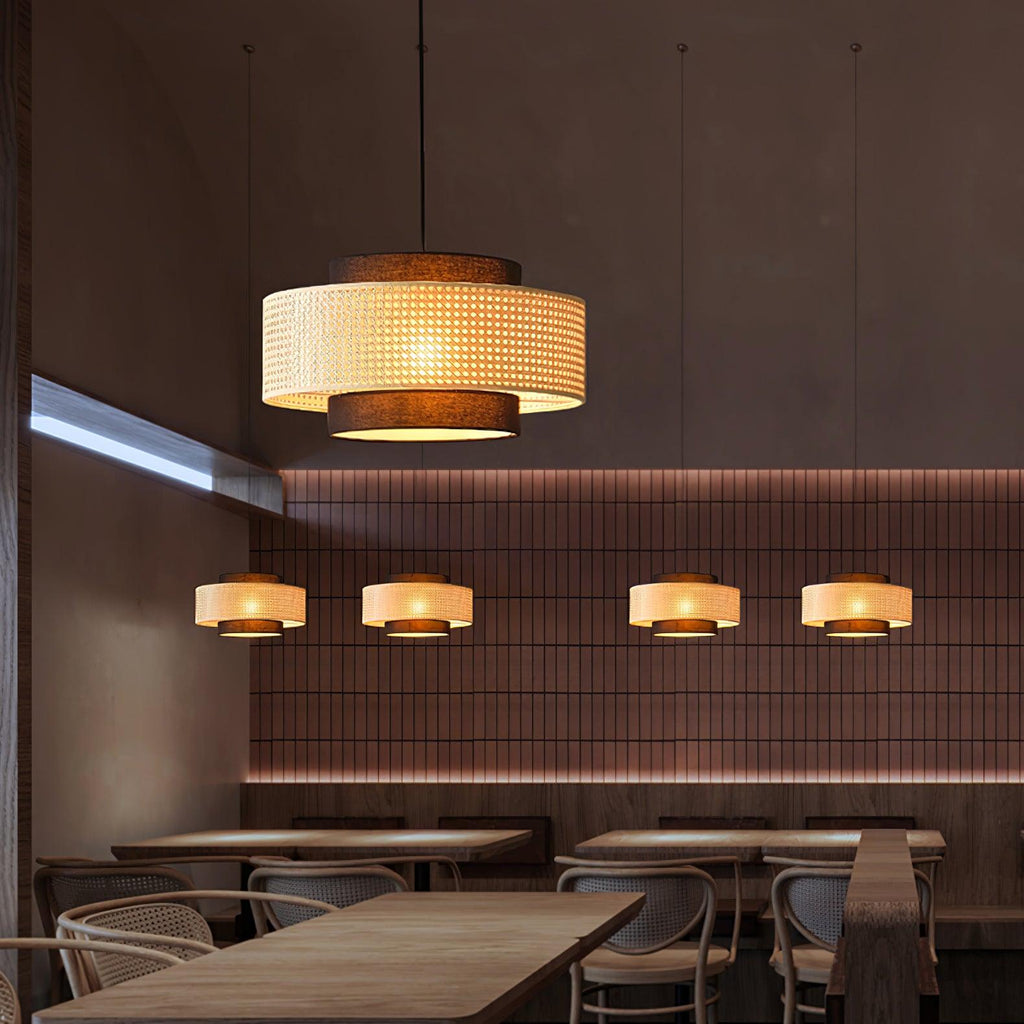 A large Clérachic rattan pendant hangs close to the camera, with smaller ones glowing in a row above a bar of tables.