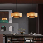 Two rattan Clérachic pendants hang above a dark dining table with woven-back chairs and a vase of branches.