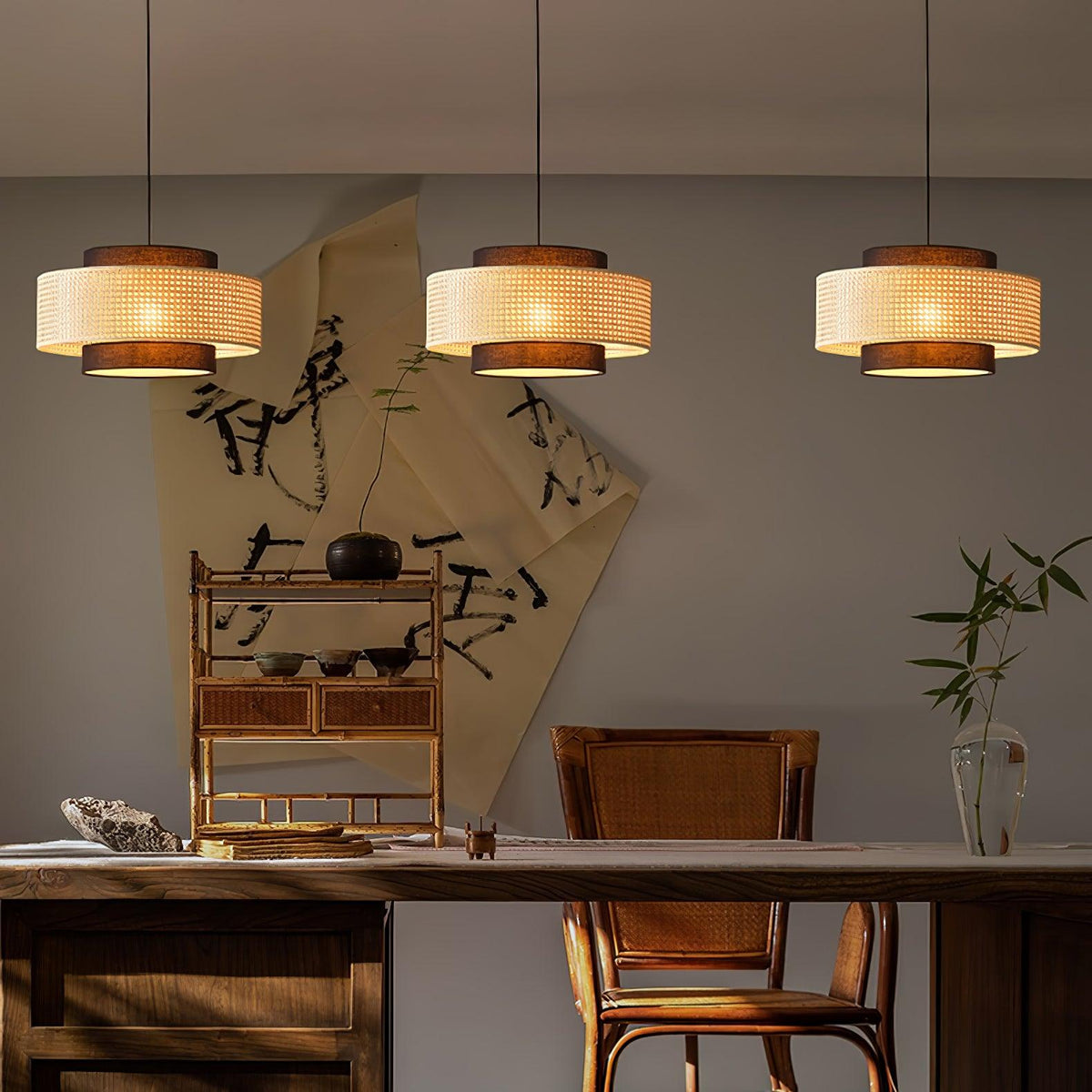 Three Clérachic pendants with woven rattan drums hang in a row, in front of a calligraphy scroll and a wooden desk.