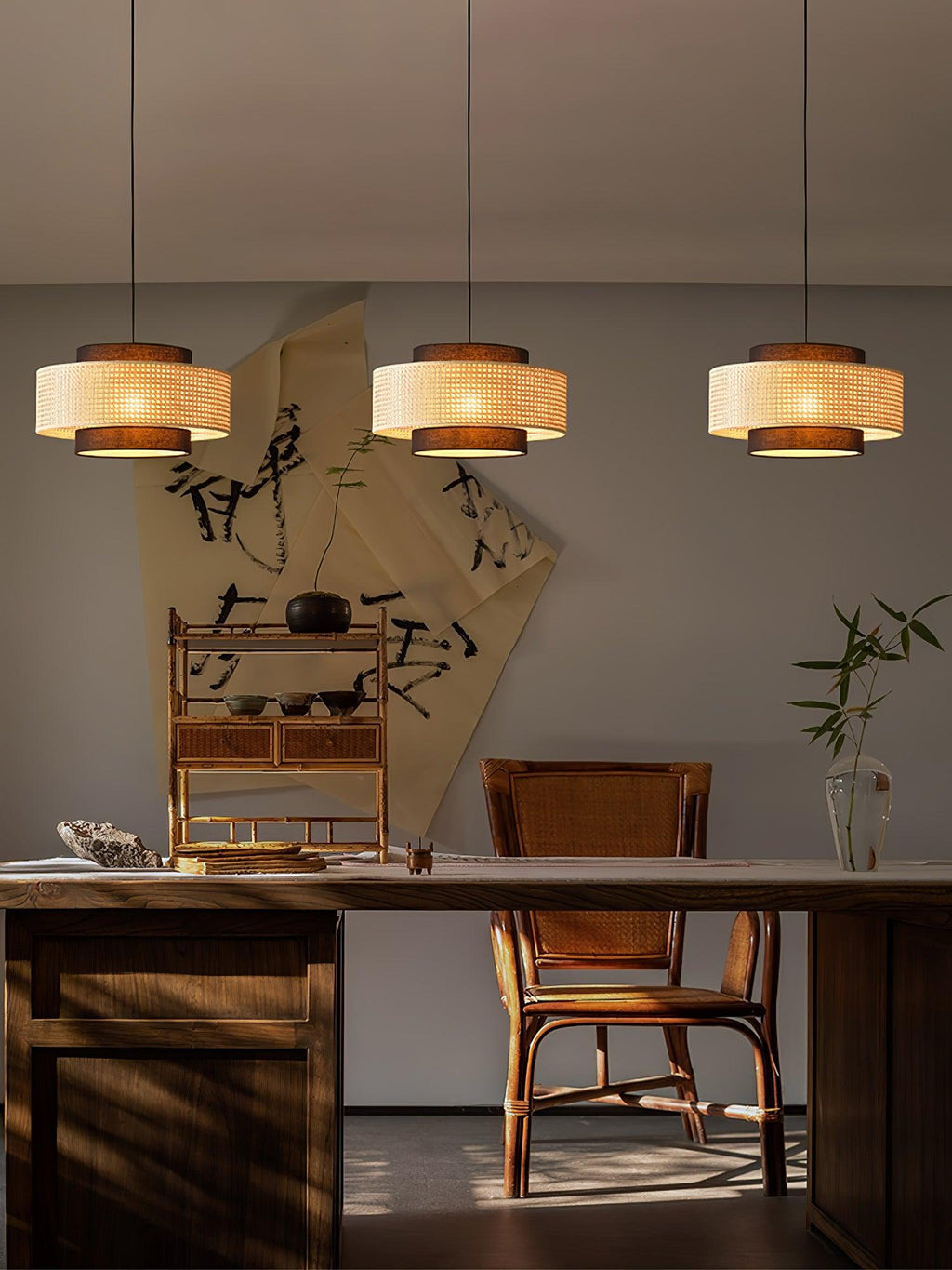 The same three rattan Clérachic pendants seen from further back, above a wooden desk with a cane-back chair.