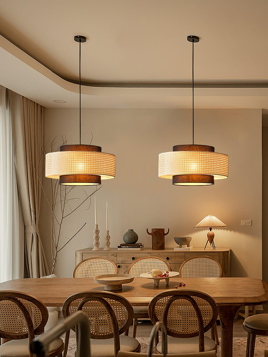 Two Clérachic rattan pendants glow over a wooden table with bentwood chairs, beside tall curtains and a sideboard.