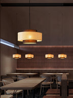 A rattan Clérachic pendant hangs in the foreground of a restaurant, with smaller ones lit in a line behind it.