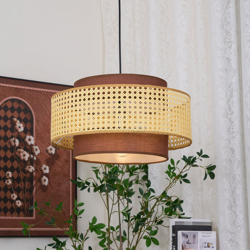 A rattan Clérachic pendant seen from just below, with a framed print and a green branch in front of lace curtains.