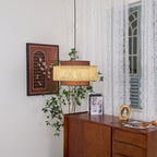 The same corner with the Clérachic pendant seen slightly closer, above a sideboard with a small gold frame and a book.