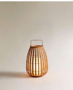 Clérachic slatted natural-fibre floor lantern with a slim metal handle, glowing warmly from a pillar light inside, small size.