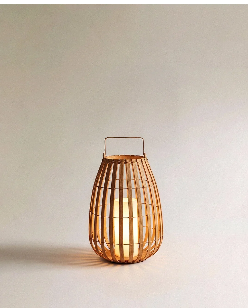 Clérachic slatted natural-fibre floor lantern with a slim metal handle, glowing warmly from a pillar light inside, small size.