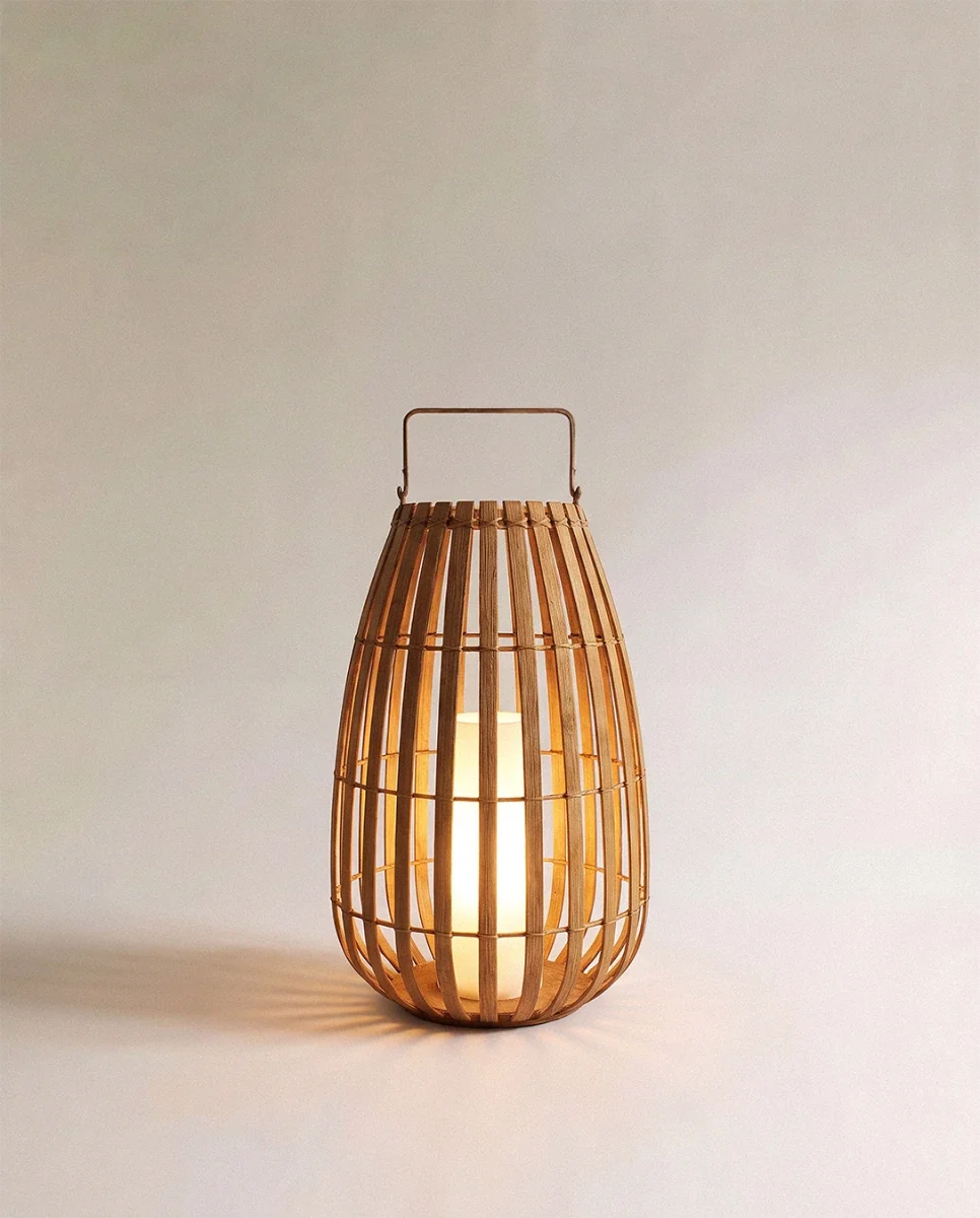 Clérachic slatted natural-fibre floor lantern with a metal top handle, lit softly by an inner pillar light, medium size.