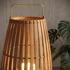 Close view of Clérachic slatted lantern with brass-toned handle and bound rim, set against a concrete wall and monstera leaves.