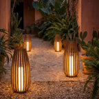 Clérachic tall slatted floor lanterns glowing at dusk on a stone path beside terracotta walls, cacti and ferns.