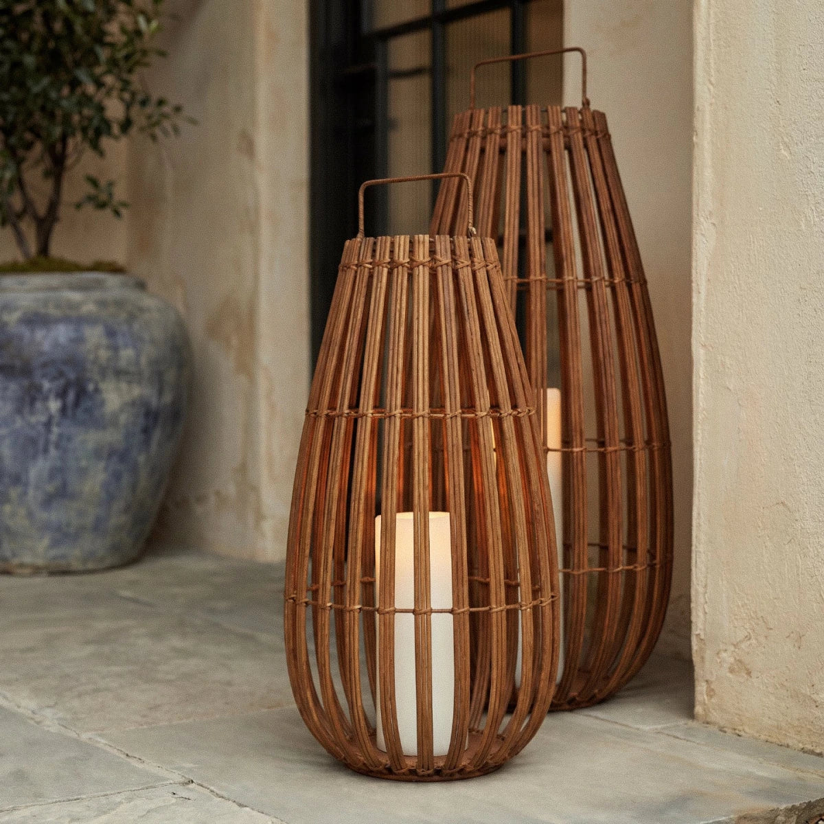 Clérachic pair of slatted lanterns with white pillar lights, one larger, set on a stone porch beside a glazed urn.