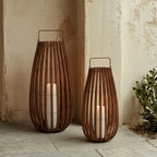 Two Clérachic slatted lanterns in different heights, each with a pillar light, standing against a weathered limewash wall.