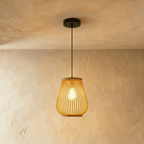 Clérachic small slatted pendant light in a rounded teardrop shape, lit warm, hanging on a black cord from a plaster ceiling.
