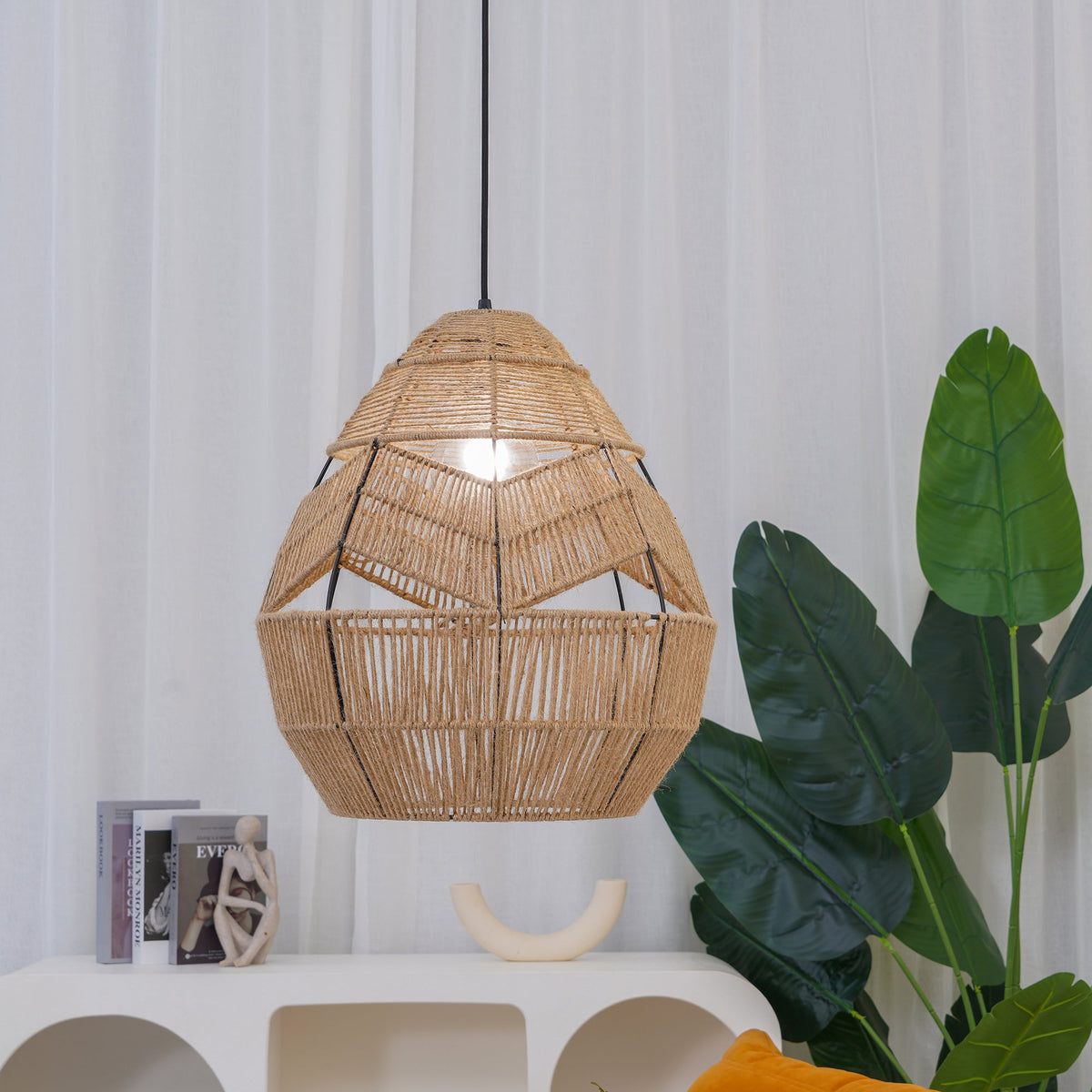 Close shot of a Clérachic woven teardrop pendant lit from within, with a large green leaf and a white shelf behind.