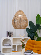 This Clérachic rattan pendant hangs beside a tall leafy plant, above a white arched shelf and an orange lounge chair.