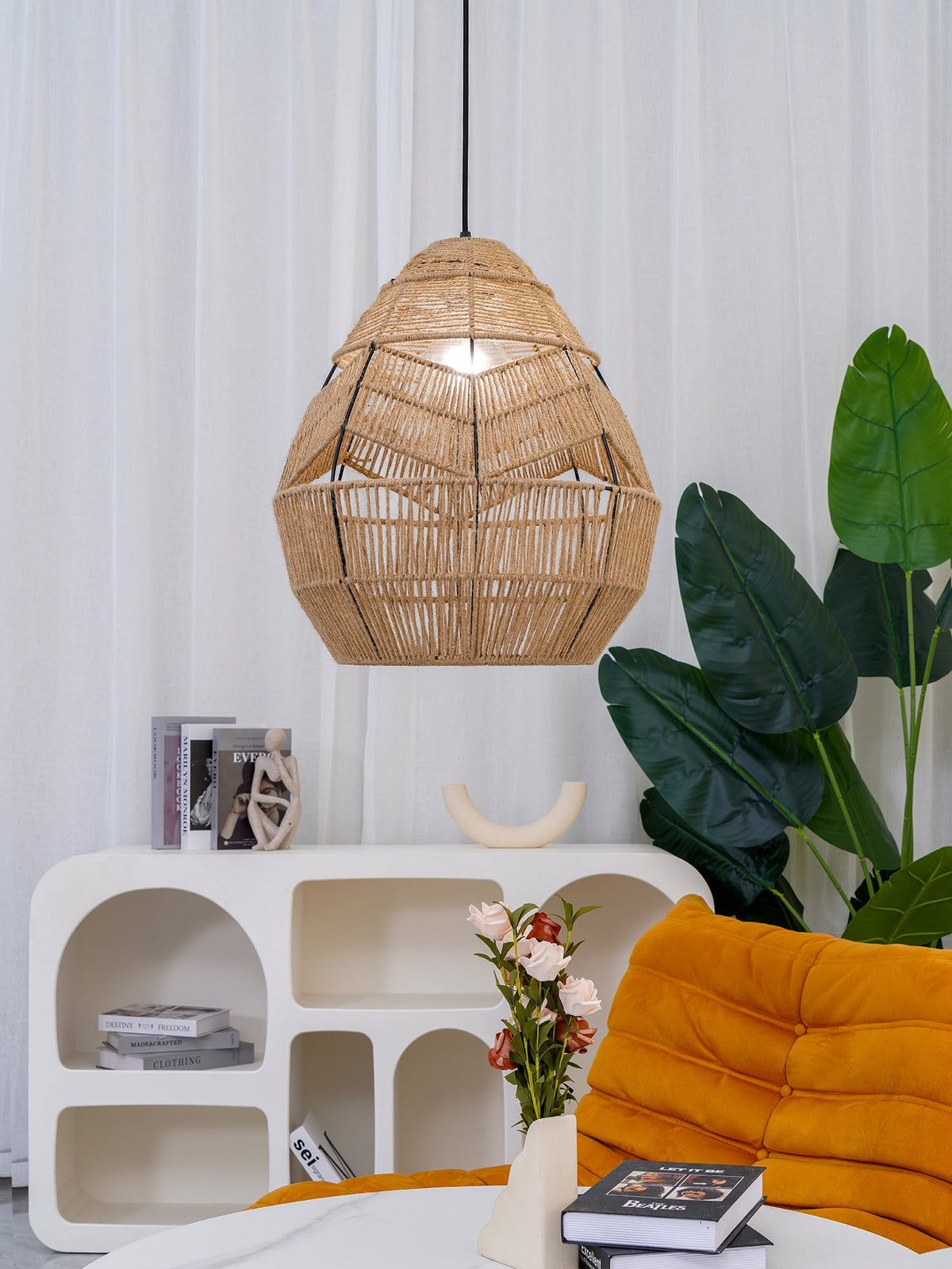 This Clérachic rattan pendant hangs beside a tall leafy plant, above a white arched shelf and an orange lounge chair.
