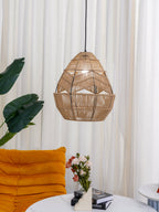 Rattan Clérachic pendant seen from a low angle, with the zigzag weave lit and an orange armchair below.