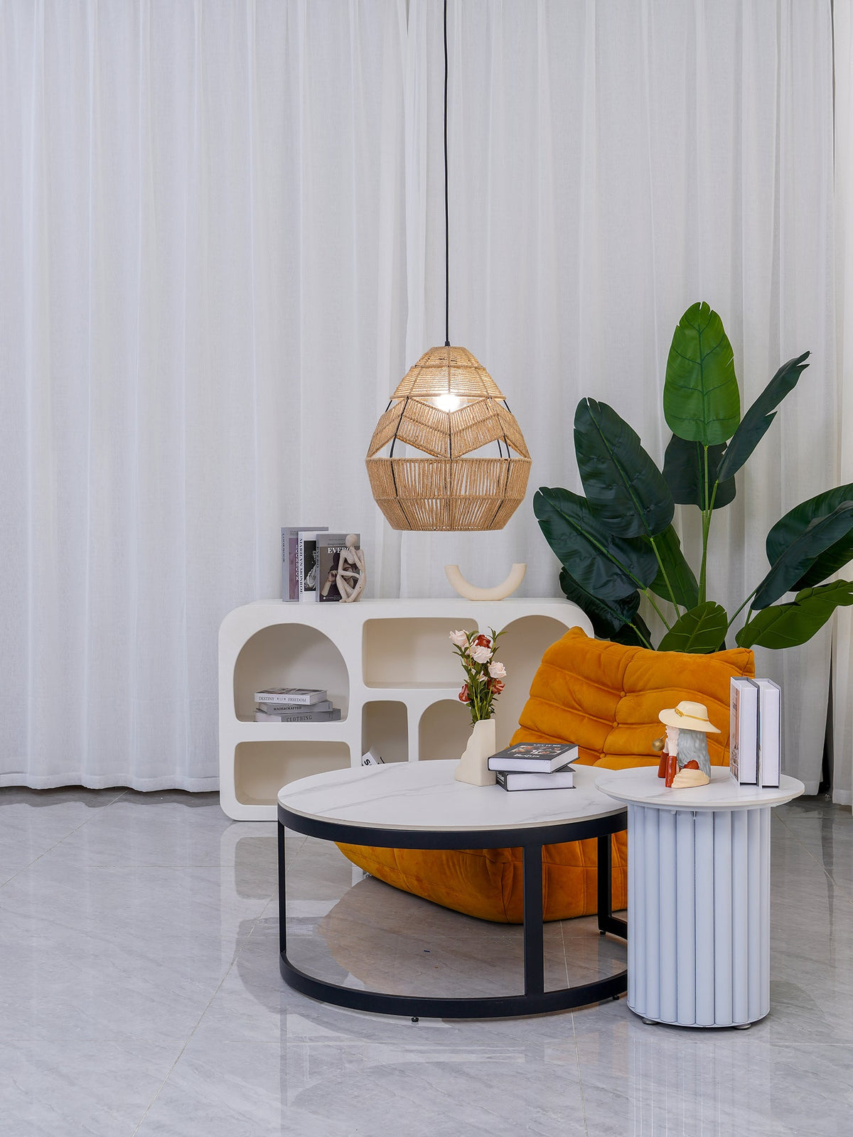 Smaller view of a Clérachic woven pendant over a round coffee table, with an orange chair and white curtains behind.