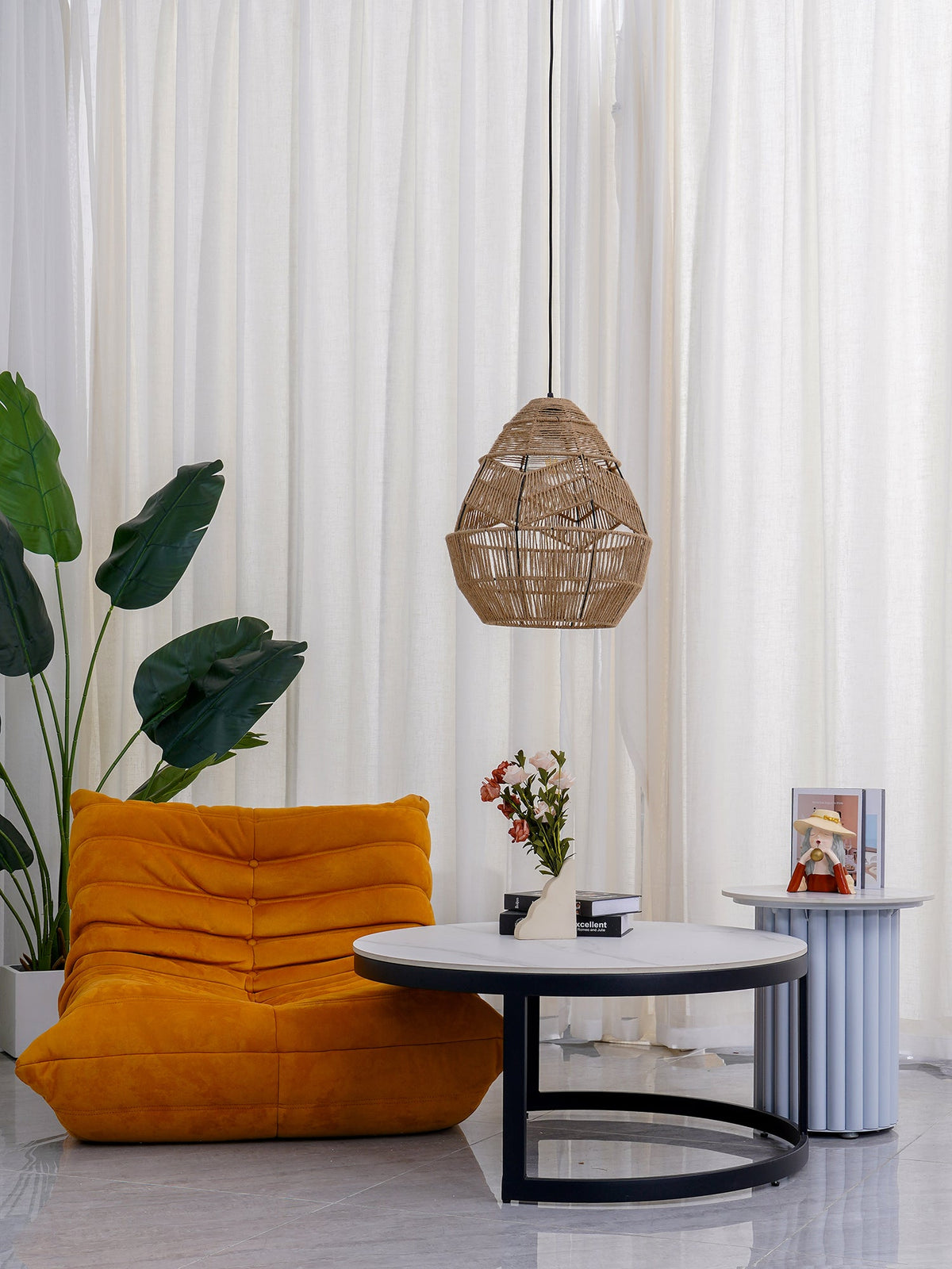 A Clérachic woven pendant hangs in a bright corner with a plant, an orange lounge chair and a low round table.