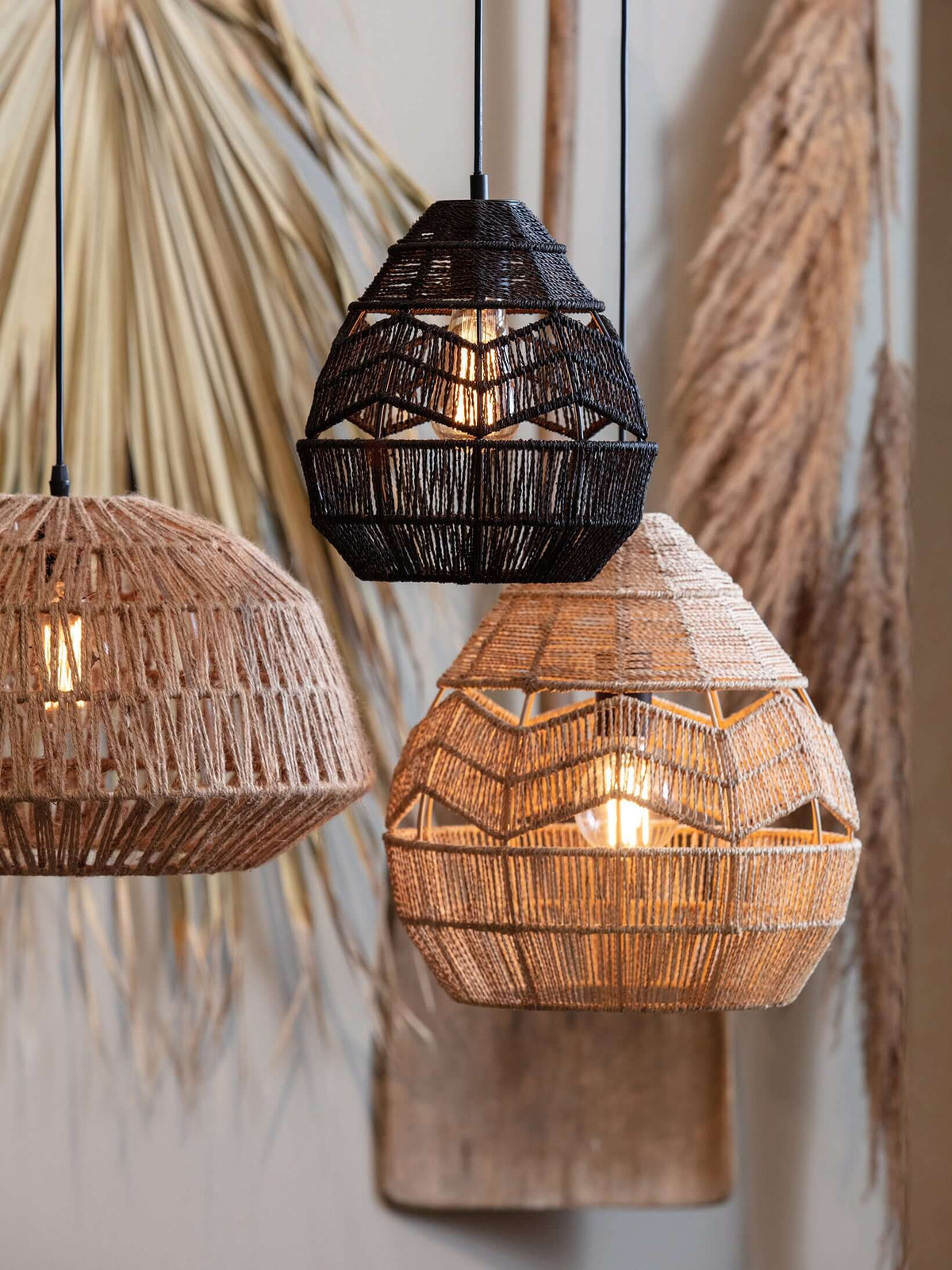 A black and a natural Clérachic woven pendant hang with a third rattan shade against dried palm and pampas.