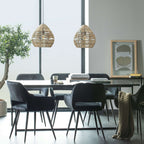 Two natural Clérachic rattan pendants hang over a black dining table and velvet chairs beside tall windows.