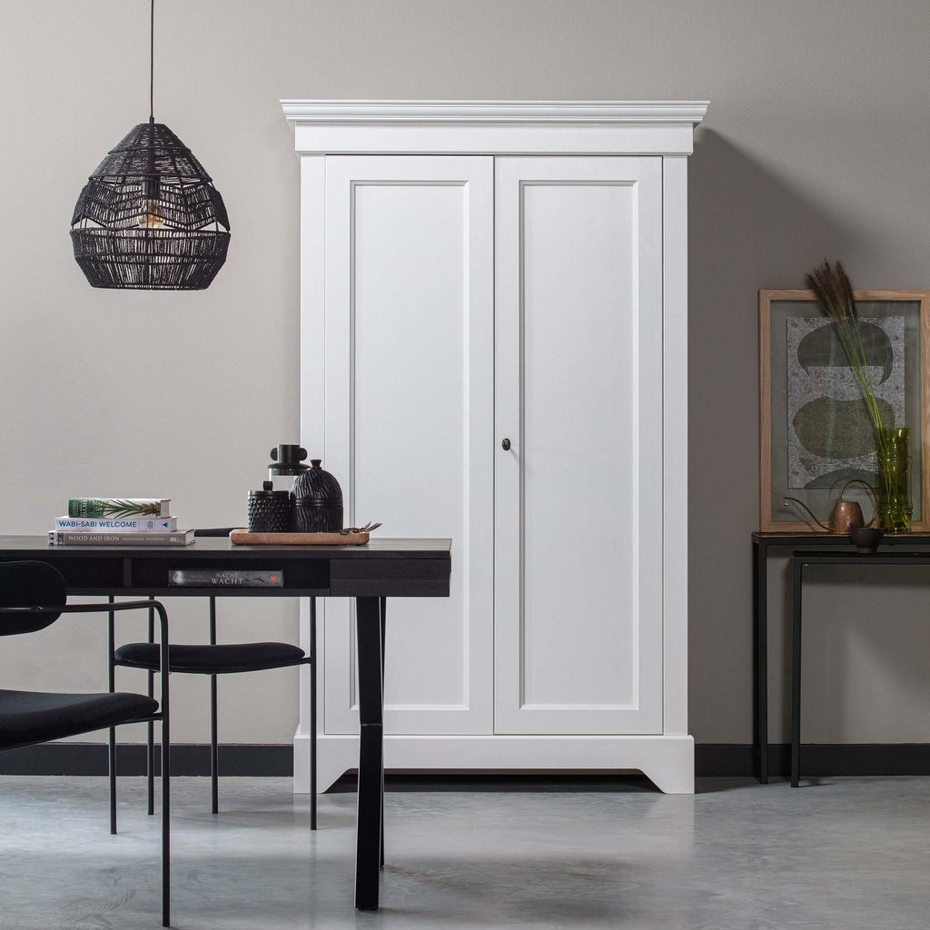 Black woven Clérachic pendant above a dark table, beside a white wooden wardrobe and a framed botanical print.