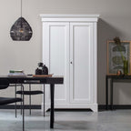Black woven Clérachic pendant above a dark table, beside a white wooden wardrobe and a framed botanical print.