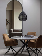 A black Clérachic woven pendant hangs under an arch over a round table with tan velvet chairs.