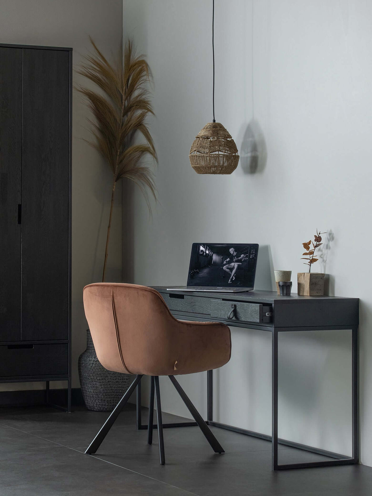 Small natural Clérachic rattan pendant above a dark desk with a tan velvet chair, beside dried pampas.