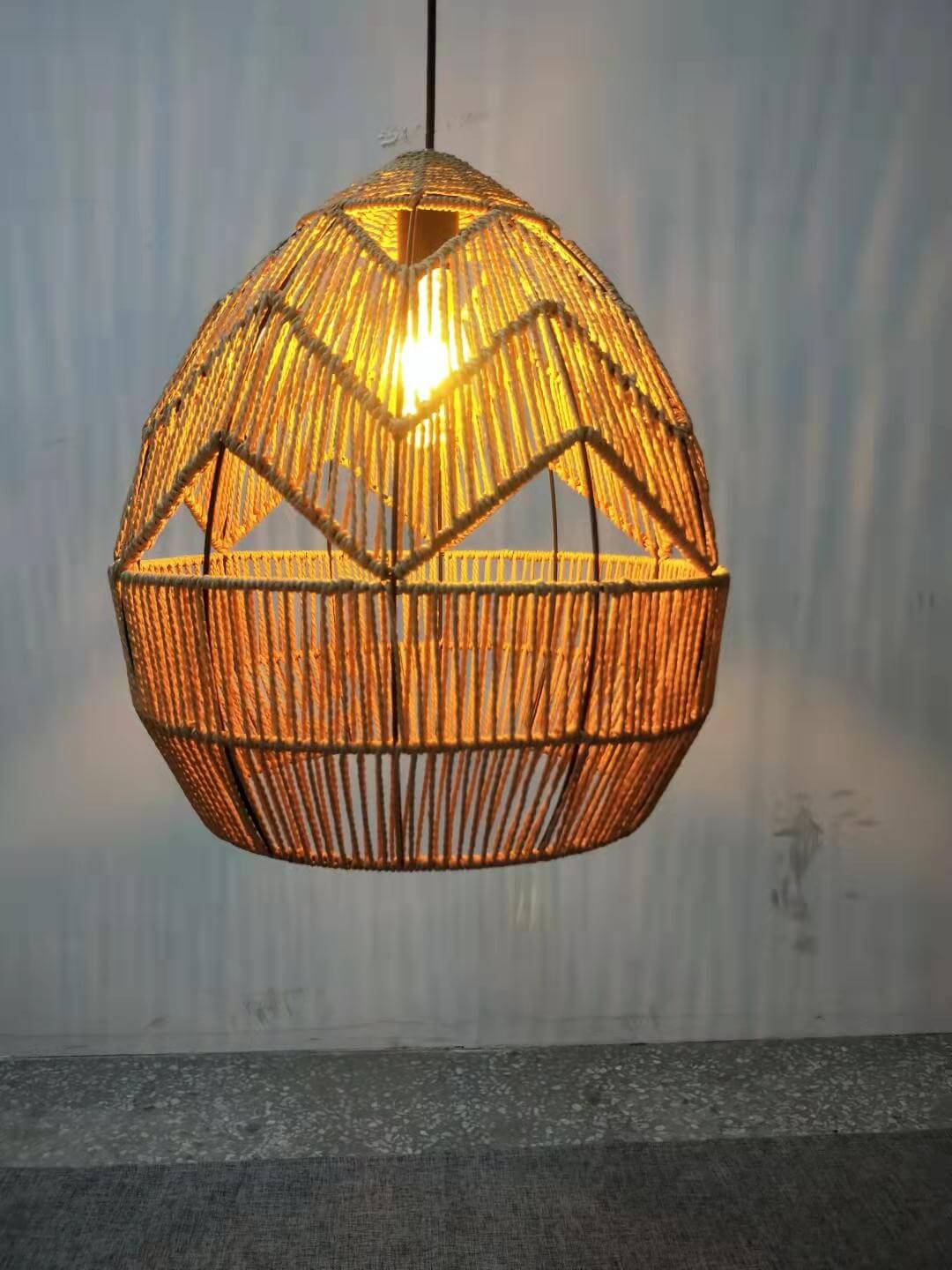 Close view of this Clérachic rattan pendant glowing amber, with the bulb visible through the zigzag openings.