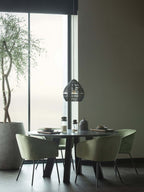 A black Clérachic woven pendant hangs far off over a round dining table with green chairs, by a tall window.