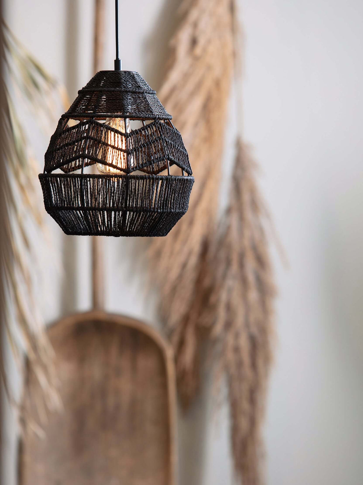 Black woven Clérachic pendant with a chevron weave, hanging in front of dried pampas and a wooden shovel.