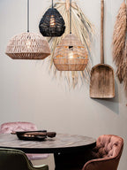 Black and natural Clérachic woven pendants hang beside a third rattan shade, above a dark round table with pink chairs.
