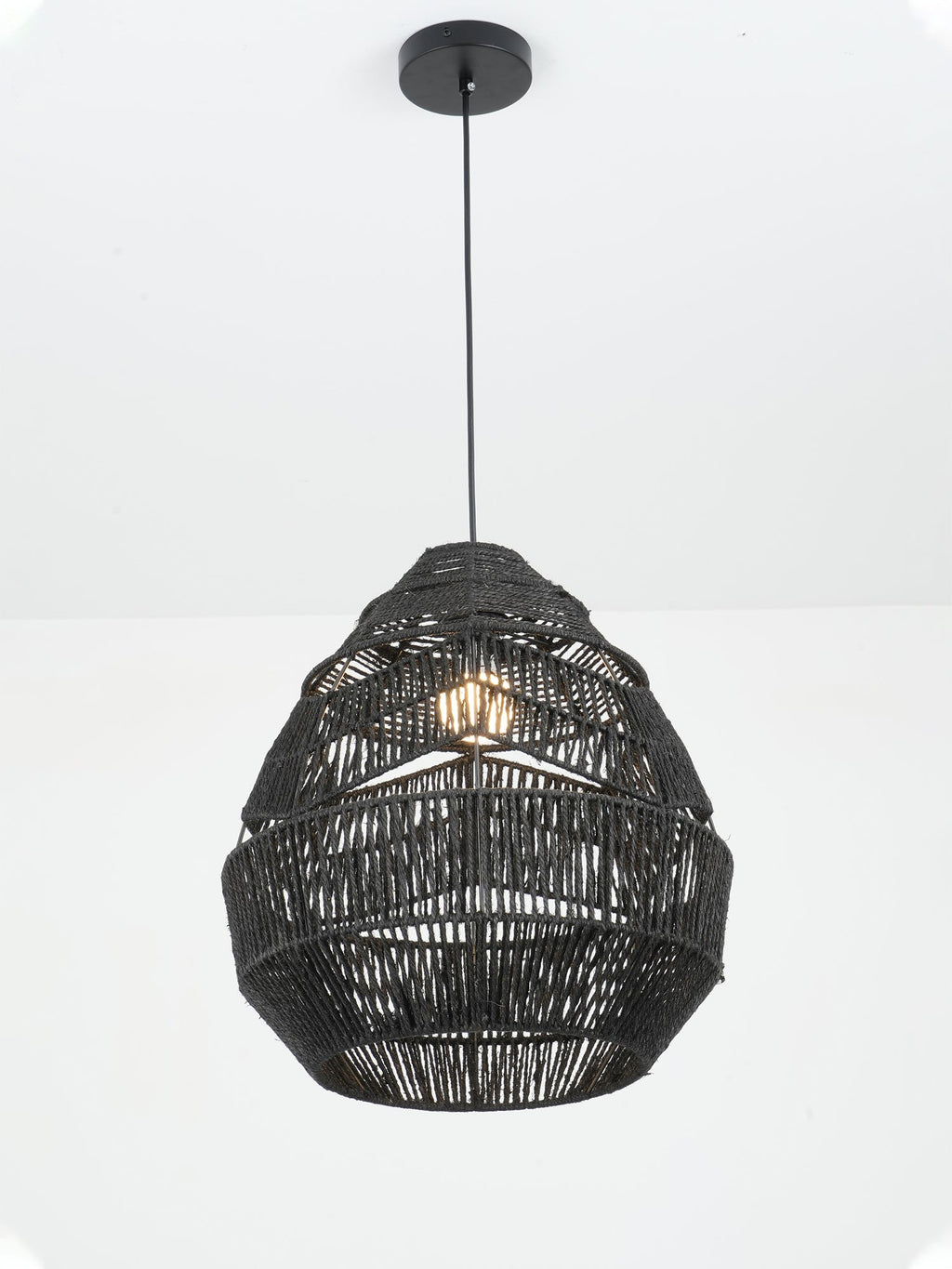 Black Clérachic woven pendant, lit, hanging from a round black canopy against a plain white wall.