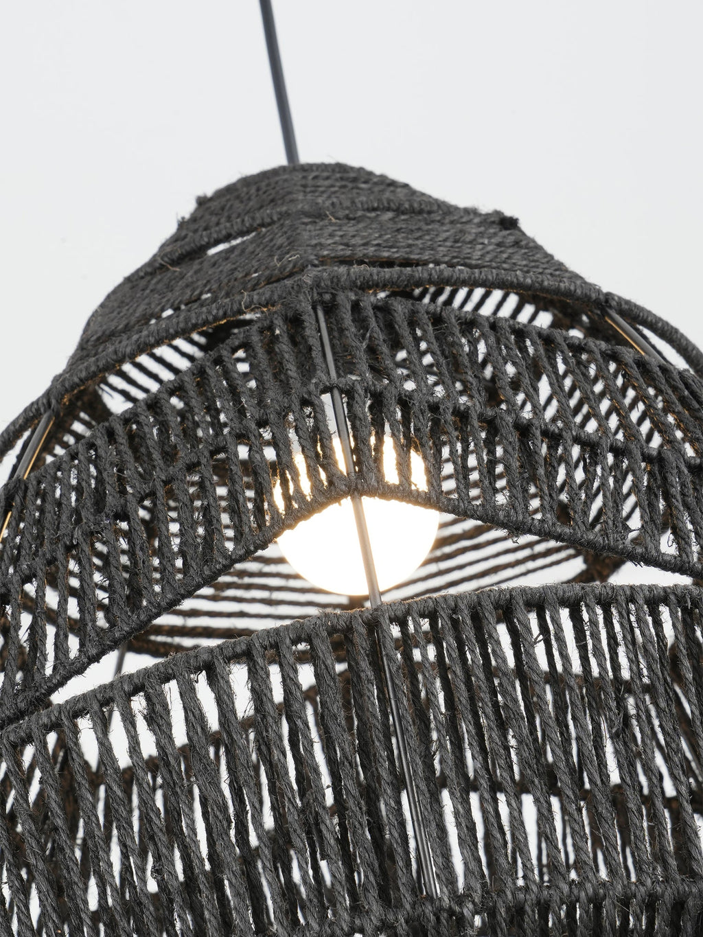 Close view of the bulb glowing inside the black woven shade of this Clérachic pendant.