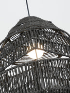 Close view of the bulb glowing inside the black woven shade of this Clérachic pendant.
