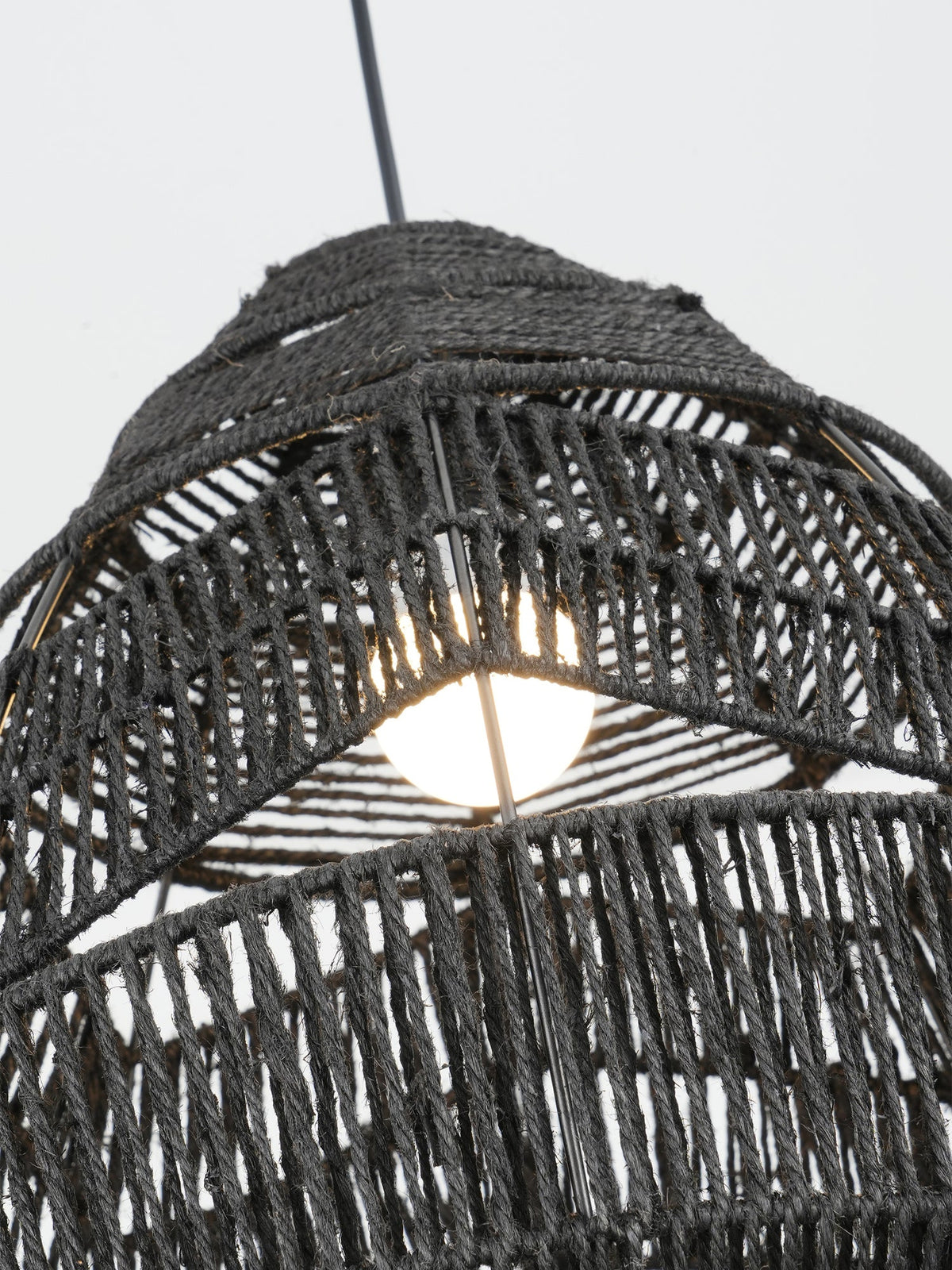 Close view of the bulb glowing inside the black woven shade of this Clérachic pendant.