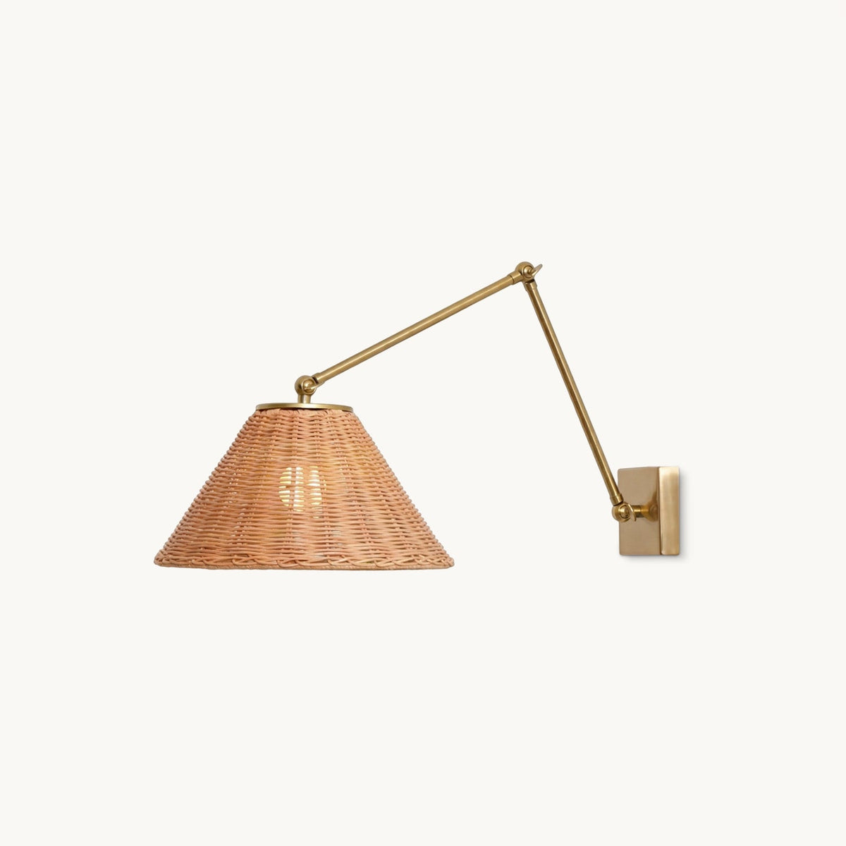 A Clérachic wall light on a plain white backdrop: a woven rattan cone shade on a gold jointed arm with a square gold wall plate.