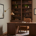 Above a study desk with a leather chair and a tall bookcase, a Clérachic rattan wall light swings out on a slim gold arm.