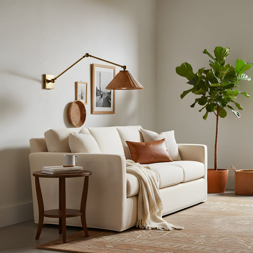 Over a cream sofa and a round side table, a rattan-shaded Clérachic wall light stretches on a long gold arm beside a framed print.