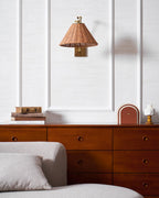 Folded close to the wall, this Clérachic rattan wall light hangs above a walnut chest of drawers on a white panelled wall.